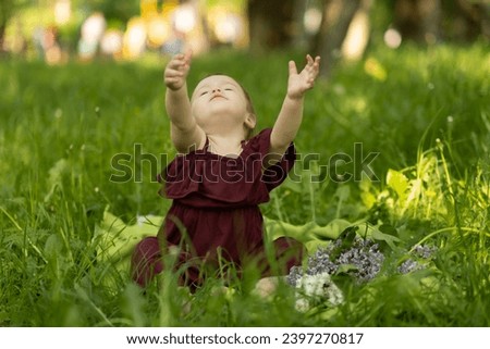 Surrounded by a halo of sunlight, a little one revels in the lush grass, her smile as bright as the day. It captures the essence of innocent merriment in nature.