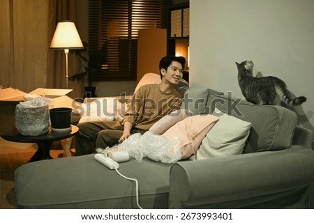 Surrounded by moving boxes, a man pauses to engage playfully with his pet cat in the evening light.