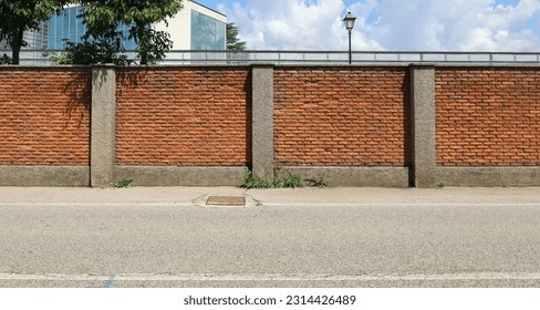 Surrounding brick wall with concrete columns with cloudy sky, street lamp and modern building on behind. Urban road in front. Background for copy space. - Shutterstock ID 2314426489
