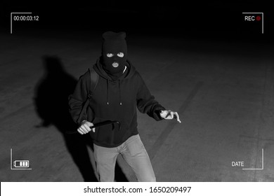 Surveillance camera caught burglar in ski mask holding crowbar while making eye contact in dark parking lot - Powered by Shutterstock