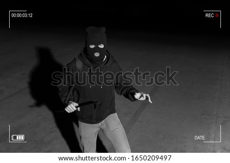 Surveillance camera caught burglar in ski mask holding crowbar while making eye contact in dark parking lot