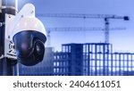 Surveillance camera at construction site. CCTV technology. Houses under construction with tower cranes. Camera for monitoring construction process. CCTV system. Camera near blurred erection building