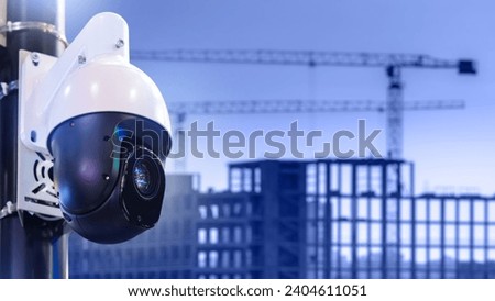Surveillance camera at construction site. CCTV technology. Houses under construction with tower cranes. Camera for monitoring construction process. CCTV system. Camera near blurred erection building