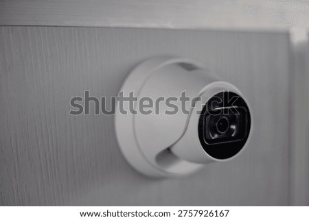 Surveillance camera mounted on wall capturing security footage in indoor environment, close up showing lens and housing, emphasizing modern monitoring technology for safety purposes