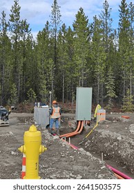 Surveyor checking trench alignment and elevation of shallow utility conduits entering electrical cabinet near hydrant.