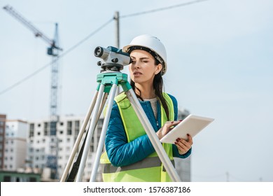 Surveyor with digital tablet looking through measuring level on construction site