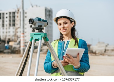 Surveyor with digital tablet and measuring level smiling at camera