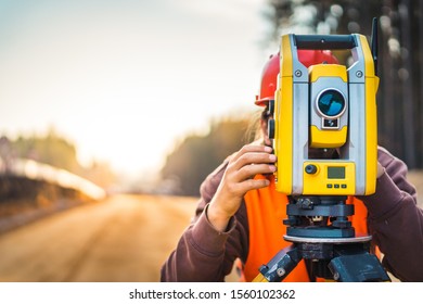 Surveyor engineer with equipment (theodolite or total positioning station) on the construction site of the road or building with construction machinery background