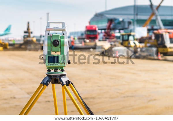 Surveyor engineer with equipment\
(theodolite or total positioning station) on the construction site\
of the road or building with construction machinery\
background