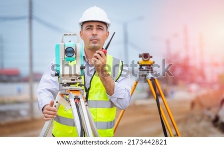 Surveyor engineer wearing safety uniform and helmet with equipment theodolite to measurement positioning and radio communication the construction site of the road with construct machinery background.