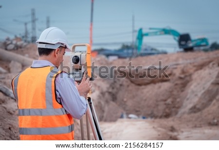 Surveyor engineers wearing safety uniform ,helmet and radio communication with equipment theodolite to measurement positioning on the construction site of the road with construct machinery background.
