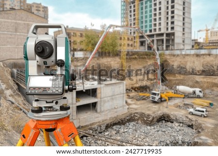 Surveyor equipment at construction site. Geodetic device on tripod. Optical theodolite near house under construction. Electronic surveyor tool. Equipment for measuring work in geodesy