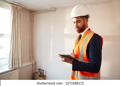 Surveyor In Hard Hat And High Visibility Jacket With Digital Tablet Carrying Out House Inspection