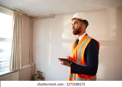 Surveyor In Hard Hat And High Visibility Jacket With Digital Tablet Carrying Out House Inspection