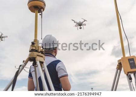 A surveyor operating a drone to conduct topographic RTK or PPK aerial survey or photography of a site. A GNSS receiver is visible in front.