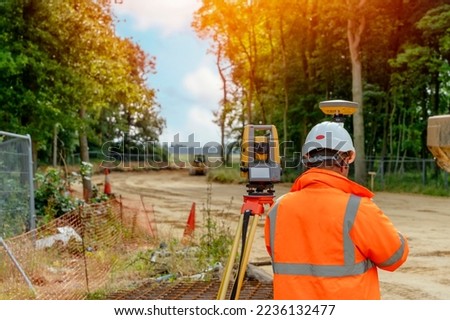 Surveyor site engineer with total positioning station on the construction site of the new road construction with construction machinery and materials  in the background