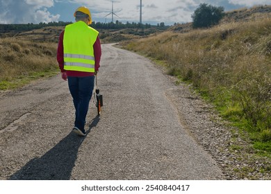 Surveyor walking and using odometer for measuring road distances with wind turbines in background