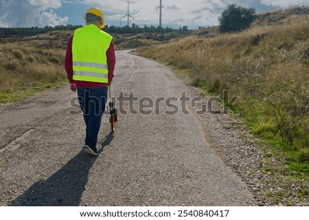 Surveyor walking and using odometer for measuring road distances with wind turbines in background