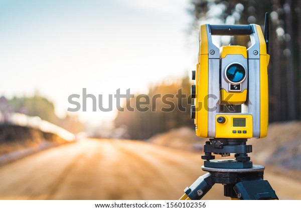 Surveyors equipment (theodolite or\
total positioning station) on the construction site of the road or\
building with construction machinery\
background