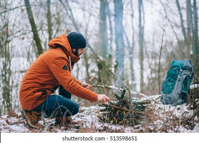 Survival Man Is Making Camp Fire In The Winter Woods