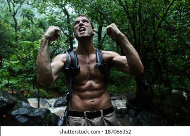 Survival Man Strong Cheering In Jungle Rainforest. Muscular Male Survivor Celebrating Cheerful In Forest At Night Showing Muscles And Aggressive Survival Instinct