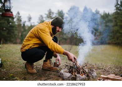 Survival in the wild. A bearded man lights a fire near a makeshift shelter made of pine branches. - Powered by Shutterstock