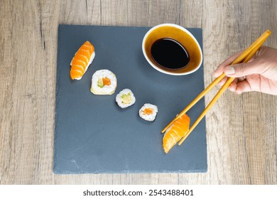 Sushi assortment Maki nigiri california roll fresh salmon avocado nori seaweed rice served on wooden table on a slate plate with soy bowl. Hand with chopsticks picking one up traditional Japanese food - Powered by Shutterstock