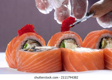 The sushi chef decorates the rolls with fish caviar. Close-up of hand and knife