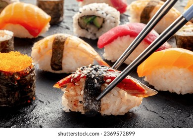 Sushi with chopsticks. Unagi sushi, nigiri with eel, and other sushi and rolls, on a black background. Japanese restaurant - Powered by Shutterstock