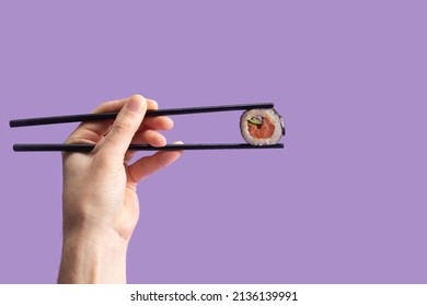 Sushi eating minimal concept. Man hand holding black chopstick with one piece rice salmon and cucumber roll in nori dried edible seaweed. Veri peri background