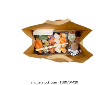 Sushi To Go Concept. Top View Of Takeaway Box With Sushi Rolls And Various Sauce Cups In Brown Paper Bag. Isolated On White, Studio Shot.