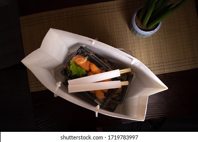 Sushi To Go Concept. Top View Of Takeaway Box With Sushi Rolls And Various Sauce Cups In Brown Paper Bag. 