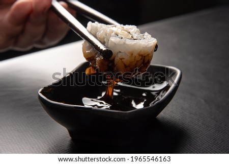 Sushi, hands picking sushi using hashi and dipping in tare sauce, black background, selective focus.