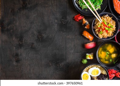 Sushi And Japanese Food On Dark Background. Sushi Rolls, Hiyashi Wakame, Miso Soup, Ramen, Fried Rice With Vegetables, Nigiri, Soy Sauce, Chopsticks. Asian/Japanese Food Frame. Overhead



