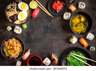 Sushi And Japanese Food On Dark Background. Sushi Rolls, Hiyashi Wakame, Miso Soup, Ramen, Fried Rice With Vegetables, Nigiri, Soy Sauce, Chopsticks. Asian/Japanese Food Frame. Overhead



