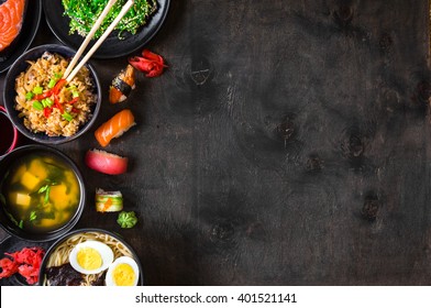 Sushi And Japanese Food On Dark Background. Sushi Rolls, Hiyashi Wakame, Miso Soup, Ramen, Fried Rice With Vegetables, Nigiri, Salmon Steak, Chopsticks. Asian/Japanese Food Frame. Overhead



