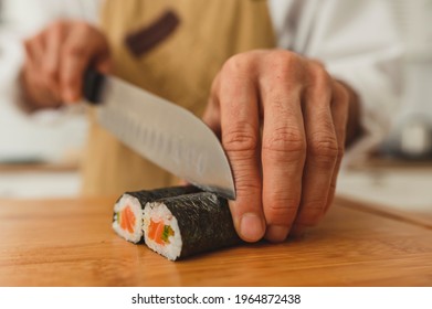 Sushi Man Makes Sushi Rolls. Wide Angle Asian Man Chef In Uniform Slice Finished Roll Into Pieces