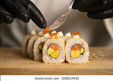 Sushi master serve Japanese roll with red salmon caviar on wooden board. Chef preparing food in protective gloves. Close up of Sushi Roll serving. Professional Cooking process. Still life. Food decor