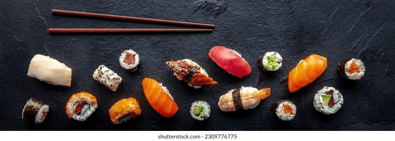 Sushi overhead flat lay panorama with chopsticks. Rolls, maki, nigiri on a black slate background, Japanese food. Salmon, eel, shrimp, tuna etc with rice - Powered by Shutterstock