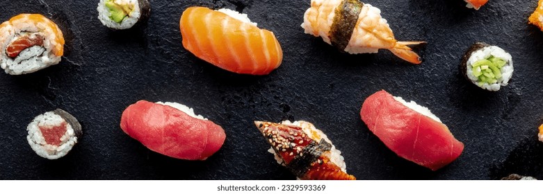 Sushi panorama. Nigiri with eel, tuna, salmon and shrimp, overhead flat lay shot on a black background, with maki and rolls. Japanese food on a plate at an Asian restaurant
