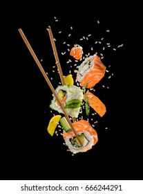 Piezas de sushi colocadas entre palillos, separadas sobre fondo negro. Comida popular de sushi.