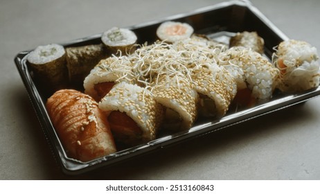 Sushi platter with various rolls and nigiri placed on concrete surface showcasing japanese cuisine in a takeout container - Powered by Shutterstock