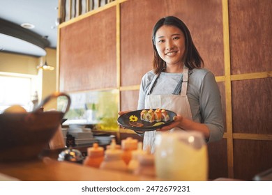 Sushi restaurant, portrait and female waitress with a plate for serving a food order with a smile. Happy, lunch and young Asian server with Japanese recipe or meal at a traditional cuisine cafe. - Powered by Shutterstock