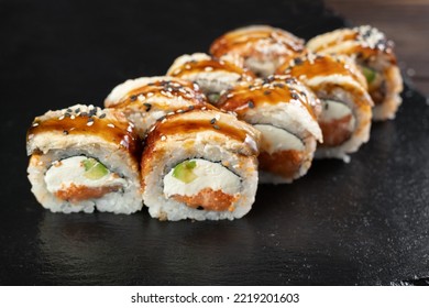 Sushi Roll With Avocado, Eel, Sesame Seeds, Sauce And Tobiko Caviar On Black Background. Japanese Cuisine, Restaurant Service. Sushi Menu Concept