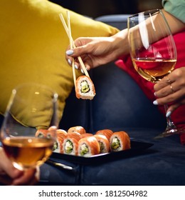 Sushi roll Philadelphia with salmon, smoked eel, avocado, cream cheese on the sofa. couple with glasses of wine. Japanese food
