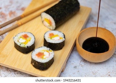 Sushi Roll With Salmon Avocado And Crab Palm With A Chopsticks And Soy Sauce Falling On A Wood Container And Stone Textured Background 