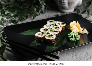 Sushi rolls with cucumber and sesame seeds served on a black plate with wasabi, pickled ginger and chopsticks - Powered by Shutterstock