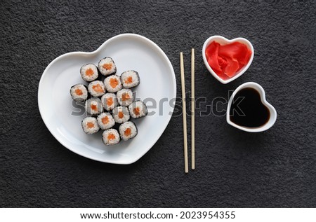 Sushi rolls with salmon, pickled ginger and soy sauce in heart-shaped plates on a dark background. Top view. A romantic dinner for Valentine's Day.