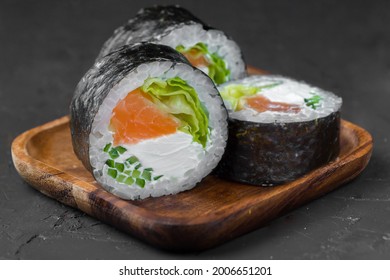 Sushi with salmon, cream cheese, cucumber, salad, nori and rice on the wooden plate on the dark background. - Powered by Shutterstock