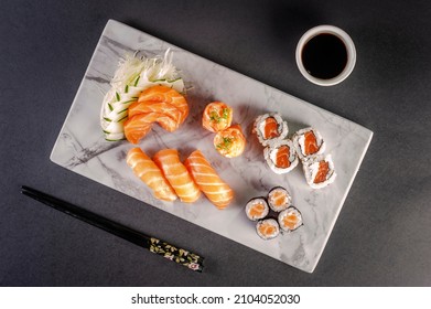 Sushi salmon varieties: sashimi, onigiri, sushi Jhow, sakemaki and uramaki philadelphia with shoyu and chopsticks on a blackbackground. Top view.